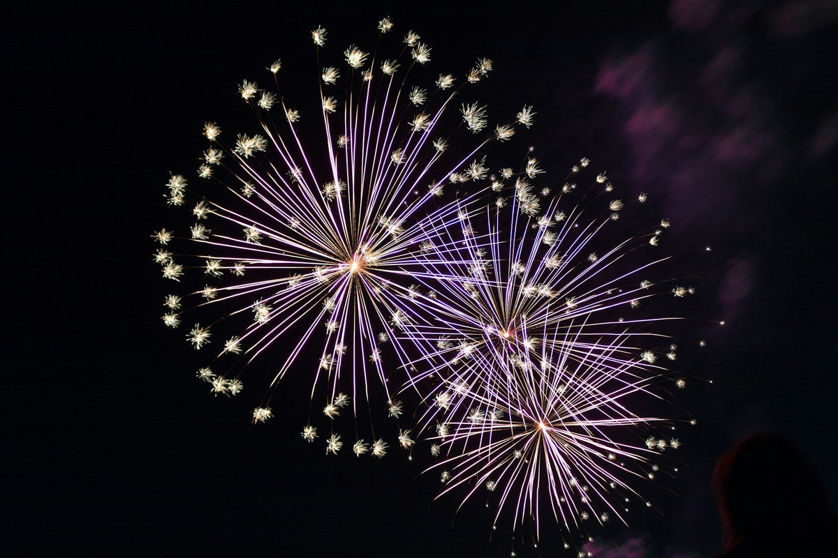 Purple and gold fireworks bursting in a night sky after a fireworks delivery order arrives