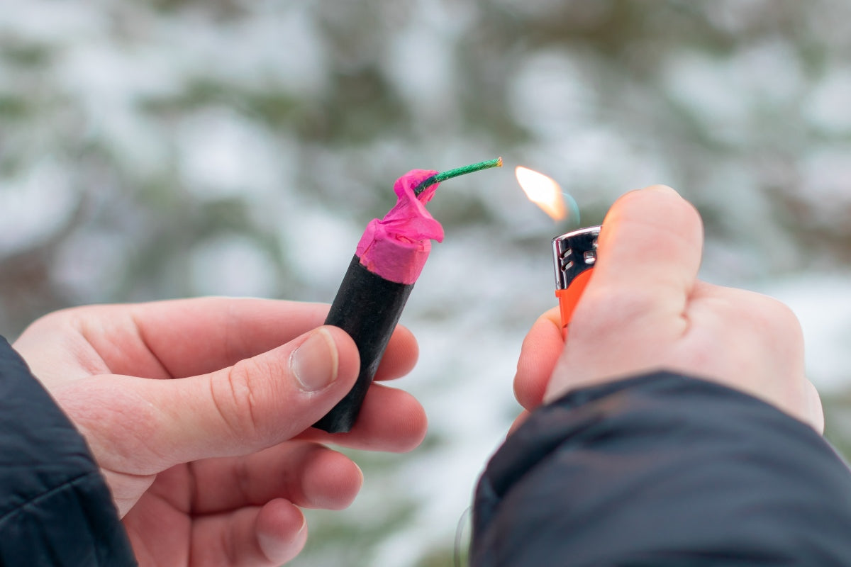 Person igniting a firecracker in winter conditions, highlighting fireworks vs hands injury risks